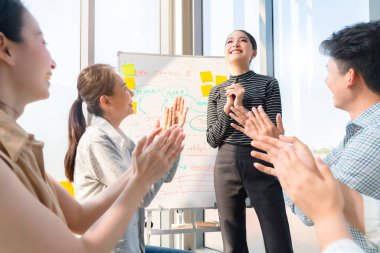 Zeki Asyalı iş kadını liderleri modern ıssız ofisteki takım arkadaşlarıyla gündelik bir toplantıda satış stratejisi ve verileri sunuyorlar ya da bir proje hedef çizelgesi için tahminlerde bulunuyorlar.