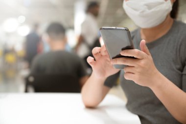 Covid19 salgınından sonra yeni normal. Zeki Asyalı kadın koruma maskesi takıyor. Mağazada akıllı telefon iletişimi kullanıyor.