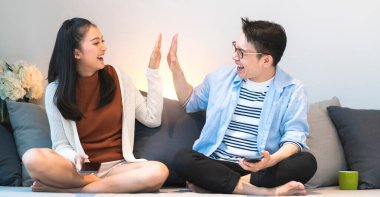 İki mutlu genç Asyalı çift hafta sonunun tadını çıkarın. Keyfinize bakın. Kanepede birlikte gülün.