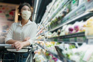 Covid salgından sonra yeni normal genç zeki Asyalı kadın süpermarkette yüz temizleme ya da maske korumalı yeni meyve sebzesi ve yeni normal yaşam tarzı seçiyor.