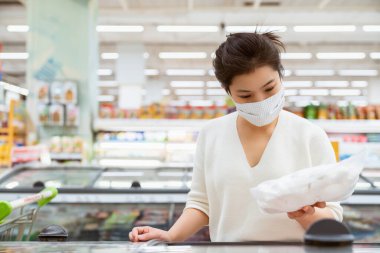 Covid salgından sonra yeni normal genç zeki Asyalı kadın süpermarkette yüz temizleme ya da maske korumalı yeni meyve sebzesi ve yeni normal yaşam tarzı seçiyor.