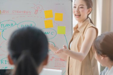 Zeki Asyalı iş kadını liderleri modern ıssız ofisteki takım arkadaşlarıyla gündelik bir toplantıda satış stratejisi ve verileri sunuyorlar ya da bir proje hedef çizelgesi için tahminlerde bulunuyorlar.