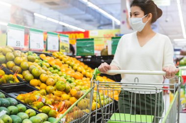 Covid salgından sonra yeni normal genç zeki Asyalı kadın süpermarkette yüz temizleme ya da maske korumalı yeni meyve sebzesi ve yeni normal yaşam tarzı seçiyor.