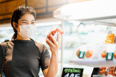 Covid salgından sonra yeni normal genç zeki Asyalı kadın süpermarkette yüz temizleme ya da maske korumalı yeni meyve sebzesi ve yeni normal yaşam tarzı seçiyor.