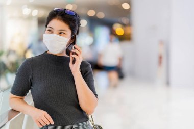 Covid19 salgınından sonra yeni normal. Zeki Asyalı kadın koruma maskesi takıyor. Mağazada akıllı telefon iletişimi kullanıyor.