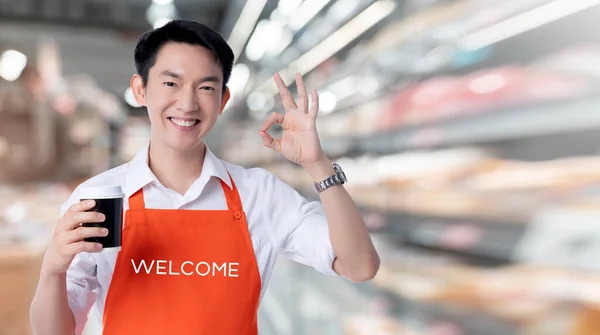 young smart attractive asian male coffeeshop business owner hand sign ok with credit card online purchase order online from home concept asian apron uniform smile warm welcome for appllication order