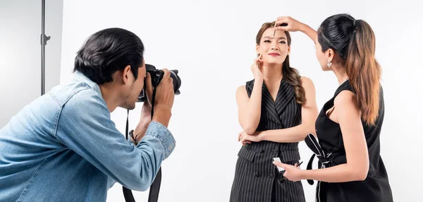 Stüdyoda profesyonel fotoğraf çekimi sahnesinin arkasında: güzel genç Asyalı bir model gülümsüyor ve makyaj sanatçısıyla poz veriyor. Makyaj fotoğrafçısı dijital bir kamerayla fotoğraf çekiyor.