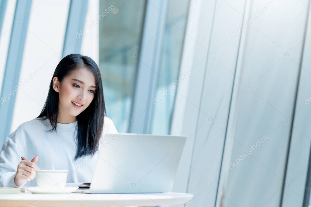 entrepreneur  startup business owner attractive asian female business woman communication with smartphone and laptop white dress cheerful and smile with confience blur office background