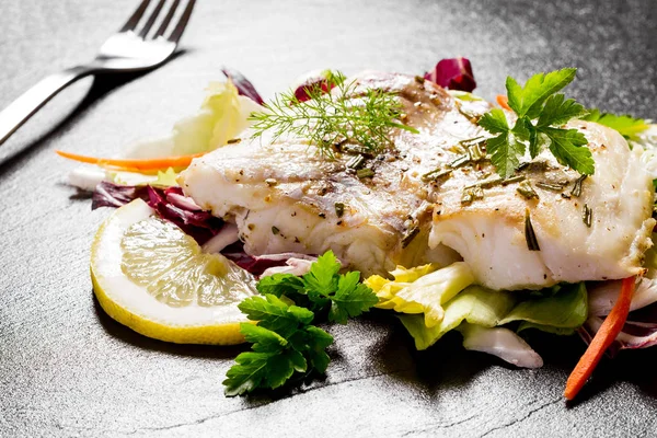 Grilled cod fillet with salad on black slate plate — Stock Photo, Image