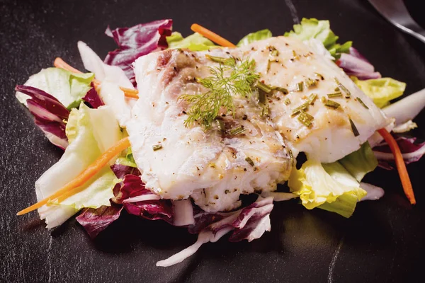 Grilled cod fillet with salad on black slate plate — Stock Photo, Image