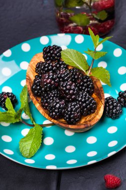 Koyu arka plan üzerinde ahşap bir gemide bir kabın içinde nane yaprakları ile olgun böğürtlen