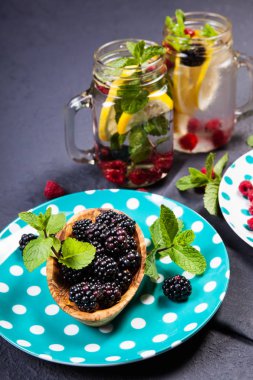 Koyu arka plan üzerinde ahşap bir gemide bir kabın içinde nane yaprakları ile olgun böğürtlen