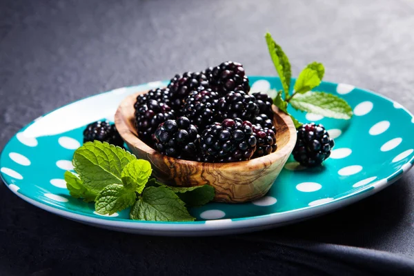 Koyu arka plan üzerinde ahşap bir gemide bir kabın içinde nane yaprakları ile olgun böğürtlen