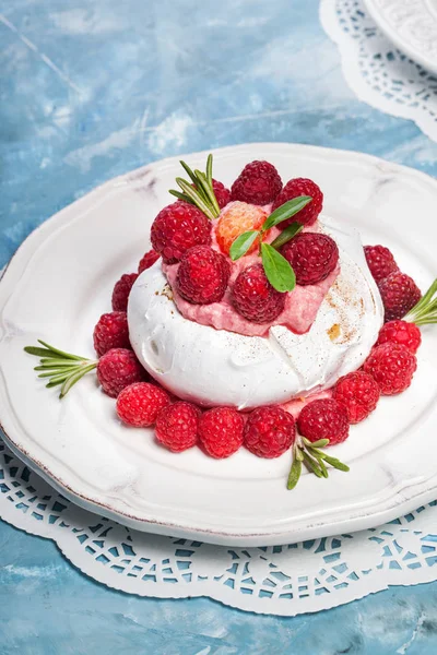 Meringue pavlova cake served with whipped cream and fresh raspberries with dripping powdered sugar