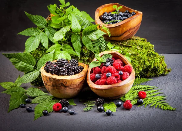 Three Wooden Bowls Blueberries Blackberries Raspberries Green Leaves Scattered Grey — Stock Photo, Image