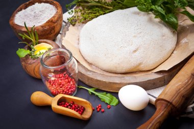 PIN, taze hazırlanmış hamuru haddeleme, döküm, un, yumurta, pembe biber ve otlar koyu gri arka plan üzerinde toz tahta