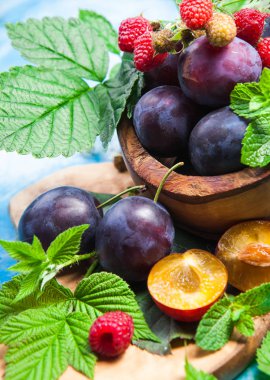 Ahşap kase tatlı Erik ve yeşil kırmızı ahududu yaprakları