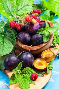 Ahşap kase tatlı Erik ve yeşil kırmızı ahududu yaprakları