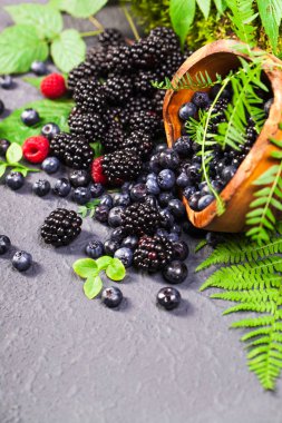 Ahşap kase taze çeşitli meyveleri. Sulu ve taze yaban mersini böğürtlen ve ahududu rustik zemin üzerine yeşil yaprakları ile. Sağlıklı beslenme ve beslenme kavramı