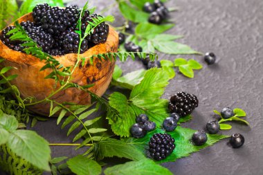 Ahşap kase taze çeşitli meyveleri. Sulu ve taze yaban mersini böğürtlen ve ahududu rustik zemin üzerine yeşil yaprakları ile. Sağlıklı beslenme ve beslenme kavramı
