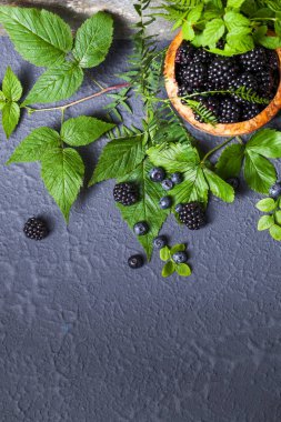 Ahşap kase taze çeşitli meyveleri. Sulu ve taze yaban mersini böğürtlen ve ahududu rustik zemin üzerine yeşil yaprakları ile. Sağlıklı beslenme ve beslenme kavramı