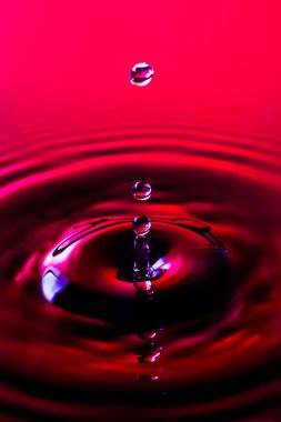 Su yüzeyi, üç su toplar ve dalgaların kırmızı bir arka plan ile havada asılı sütun sonuçlanan etkileyen bir su damlacıkları Close-up.
