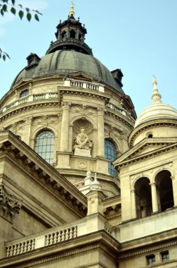 Budapeşte, Macaristan - 09.14.2019: üzerinde haçlar olan katedralin kubbeleri ve duvardaki kaidede meditasyon yapan bir aziz figürü