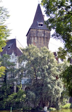 Budapeşte, Macaristan - 09.14.2019: bir ortaçağ kale binasının köşesi, gölet suyunun üzerindeki yeşil ağaçların arka planına karşı üçgen bir çatı - bir eğlence parkında sergileniyor