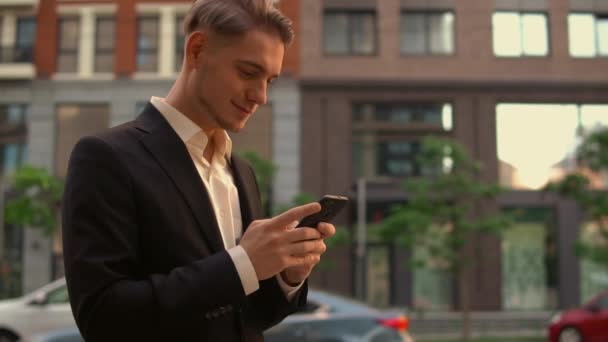 Улыбающийся бизнесмен использует мобильный телефон в городе — стоковое видео