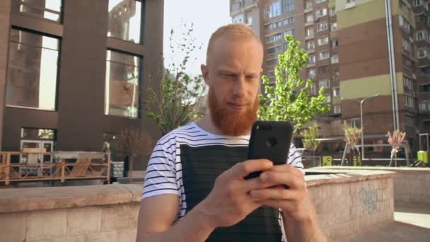 Рыжий парень прокручивает сенсорный экран телефона — стоковое видео