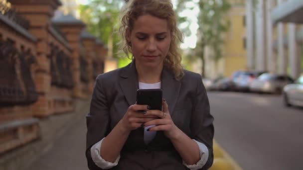 Чарівна жінка йде по вулиці і використовує свій мобільний телефон — стокове відео