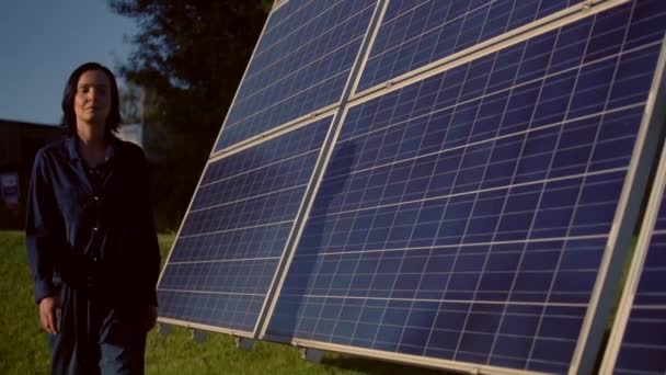 Woman wearing blue smock walks along solar batteries field — Stock Video