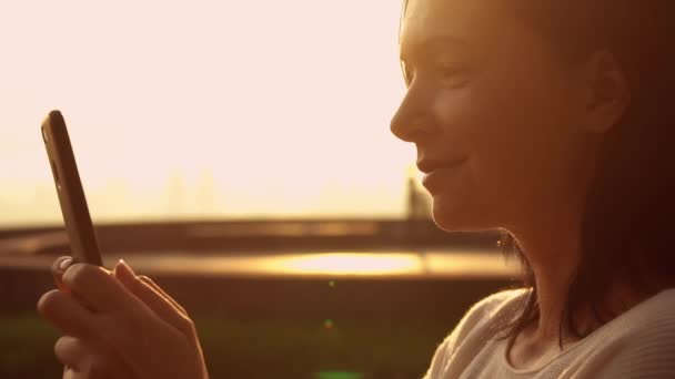 Vrouw typen op haar smarphone tegen zonsondergang op de achtergrond — Stockvideo