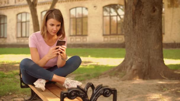 Mensagens de mulher jovem no celular perto da faculdade — Vídeo de Stock