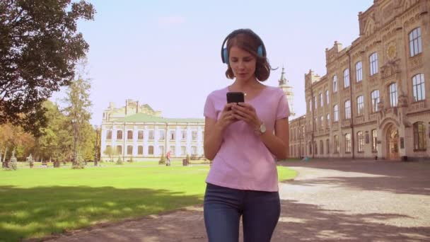 Ευτυχισμένη γυναίκα χρησιμοποιώντας ακουστικά βόλτες στην περιοχή πανεπιστημιουπόλεων — Αρχείο Βίντεο