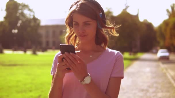 年轻女子听音乐使用智能手机走在大街上 白种人金发碧眼 穿着粉红色 — 图库视频影像