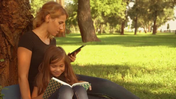 Мать, сидящая у дерева со своей дочерью — стоковое видео