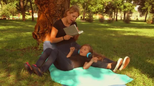 Девушка слушает музыку, пока ее мать читает книгу — стоковое видео