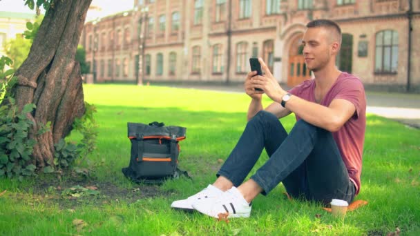 Jongeman zit in de buurt van de boom sms berichten — Stockvideo