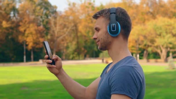 Hombre guapo con auriculares camina al aire libre — Vídeo de stock