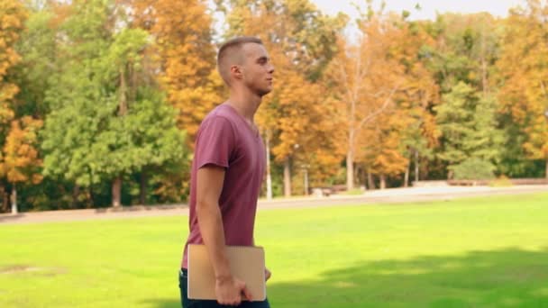 美しい自然秋スローモーションでキャンパス エリア ビューをウォーク ノートを保持している白人の学生 — ストック動画