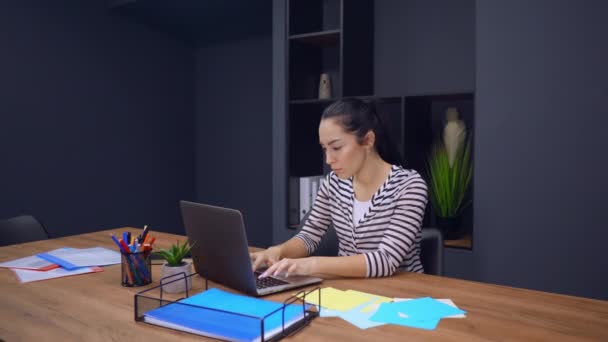 Jovem atraente trabalhando no laptop sentado na mesa de escritório interior . — Vídeo de Stock