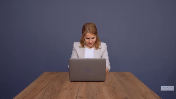 Señora de negocios de confianza está trabajando en el ordenador portátil en la mesa grande sobre fondo azul . — Vídeos de Stock