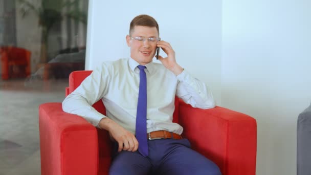 Joven hombre de negocios sentado en sillón mientras negocia por teléfono — Vídeos de Stock