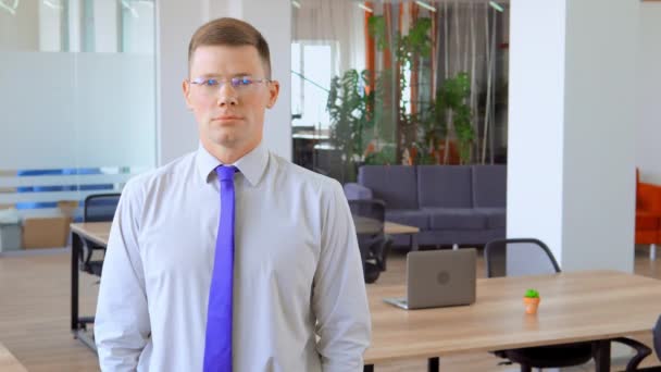 Joven con gafas sonríe en medio de la oficina — Vídeos de Stock