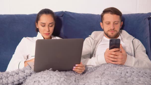 Paar is liggend onder deken en staren naar hun gadgets — Stockvideo