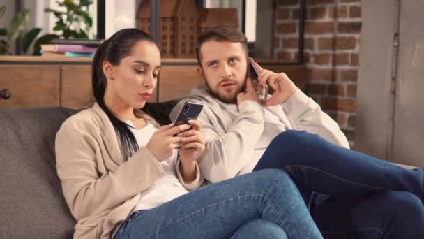 Leniví manželé sedí na gauči a používají telefony. — Stock video