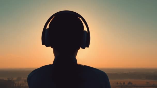 Sylwetka dziewczyna z słuchawkami stojący na wzgórzu — Wideo stockowe