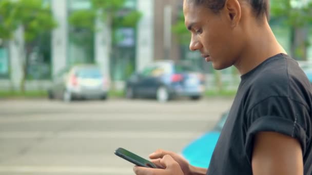 Młody człowiek stojący na ulicy za pomocą smartfona — Wideo stockowe