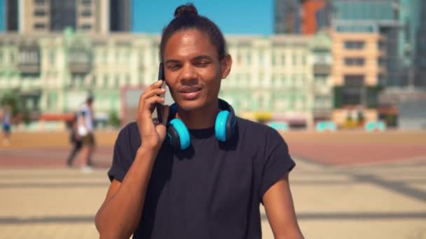 Веселый молодой человек разговаривает по телефону гуляя по улице — стоковое видео